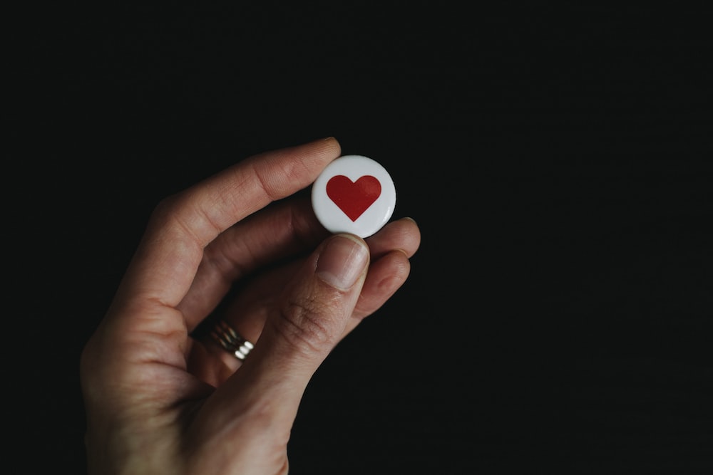 person holding red and white hear button