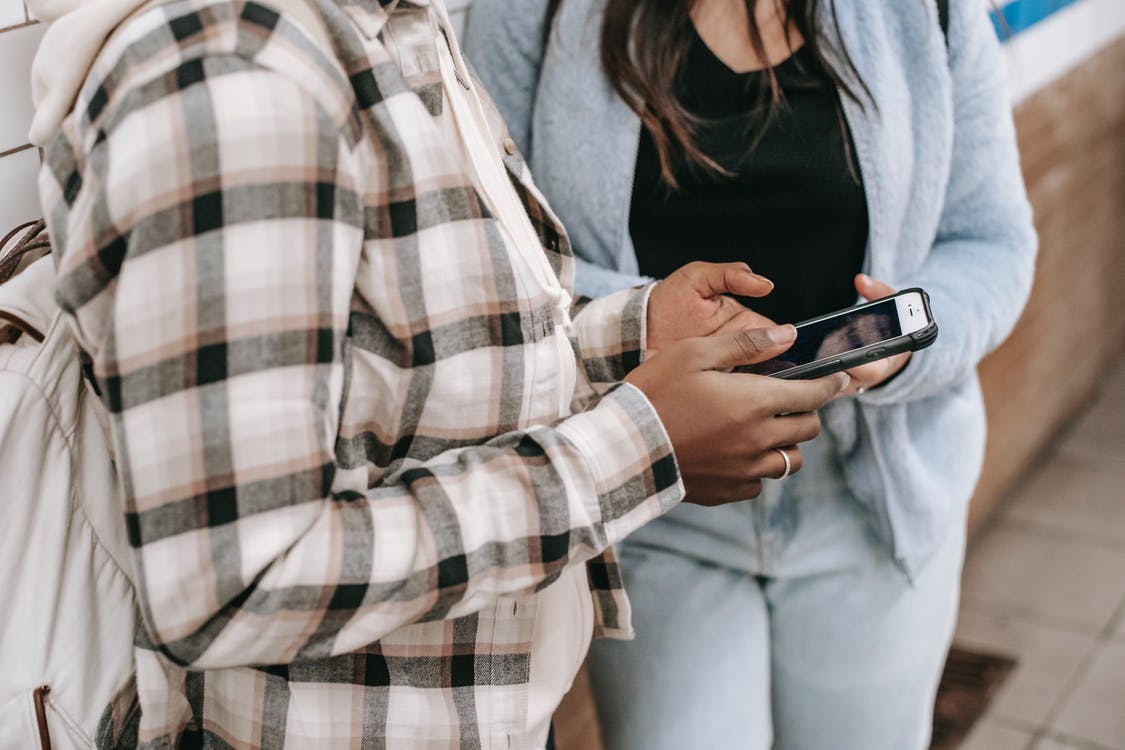 Faceless multiethnic female friends chatting on smartphone with black screen