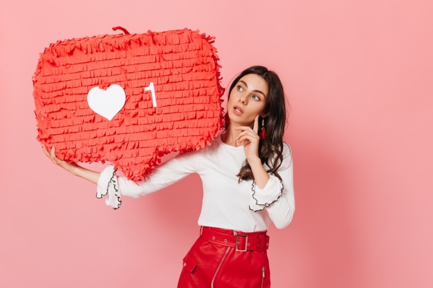 Long-haired brunette thoughtfully looks at huge red like from instagram. close-up shot of cute tanned girl. Free Photo