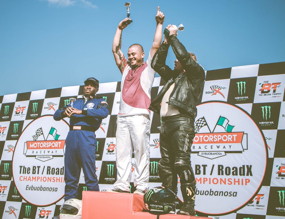 Three People Standing On Stage Holding Trophies