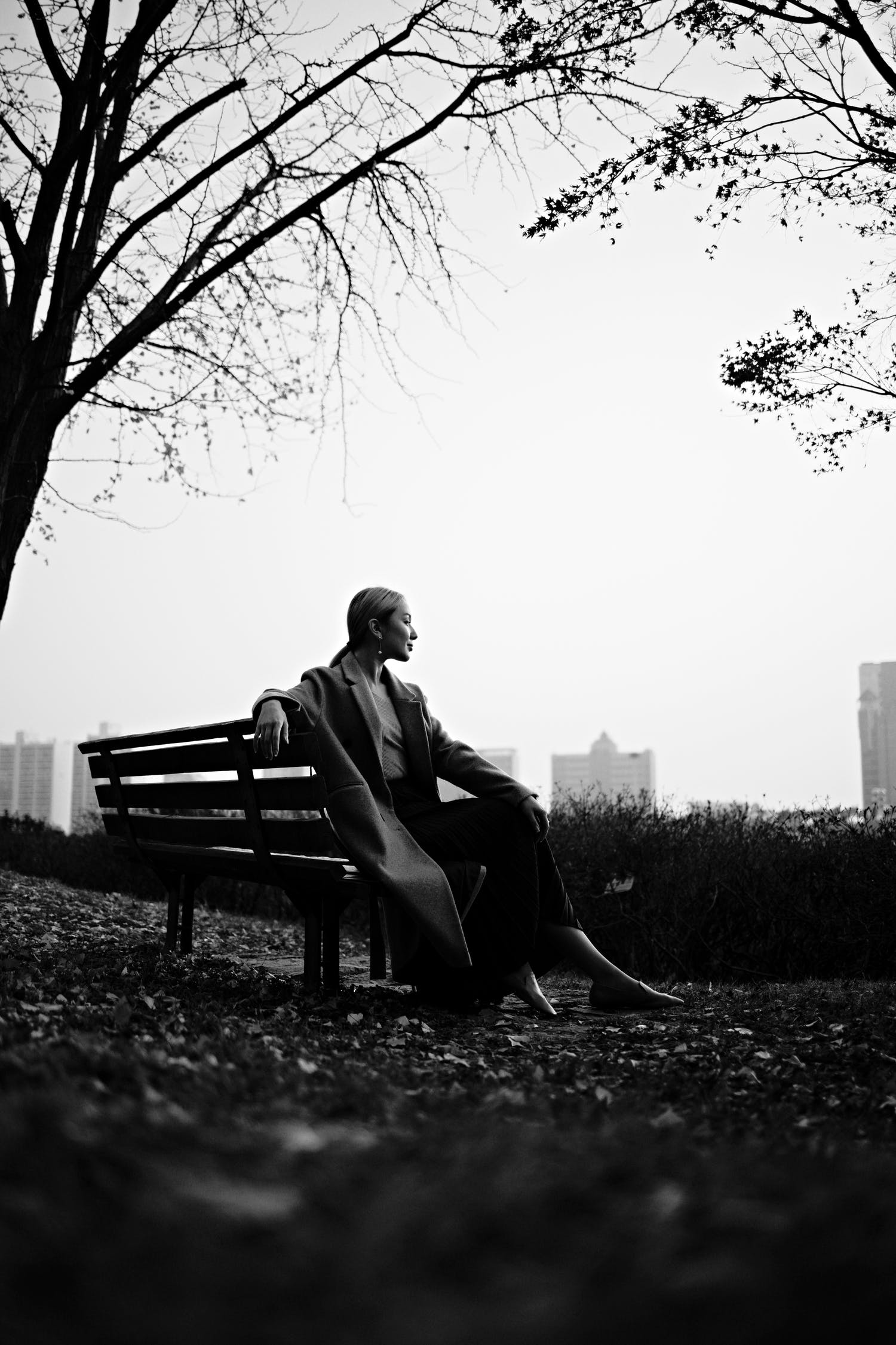 Black and white of cheerful female smiling and resting on bench of park