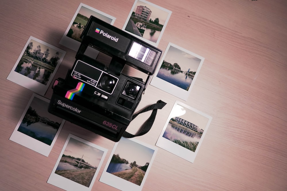 assorted photos surrounding Polaroid camera on table